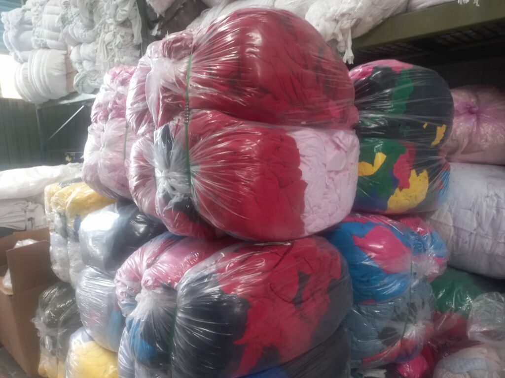 Montaña de trapo industrial México envueltas en plástico transparente dentro de una bodega industrial, listas para distribución o reciclaje textil.